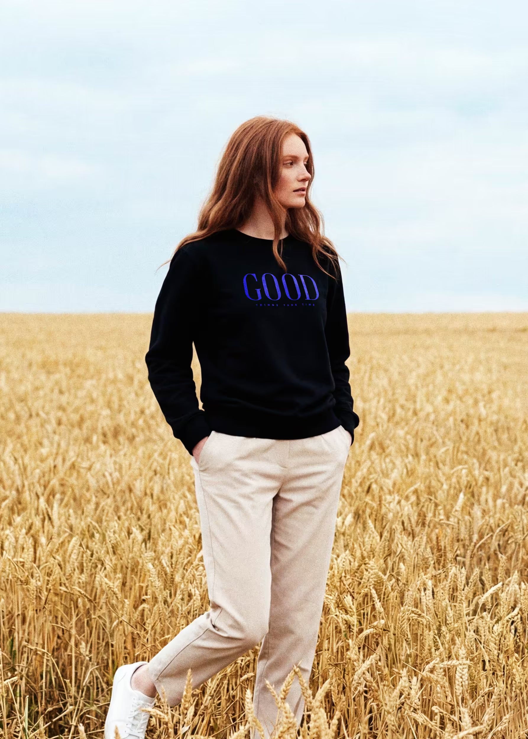 Modelo con sudadera negra Good Things Take Time en campo de trigo — serigrafía GOOD en azul eléctrico, Crystal Peppers