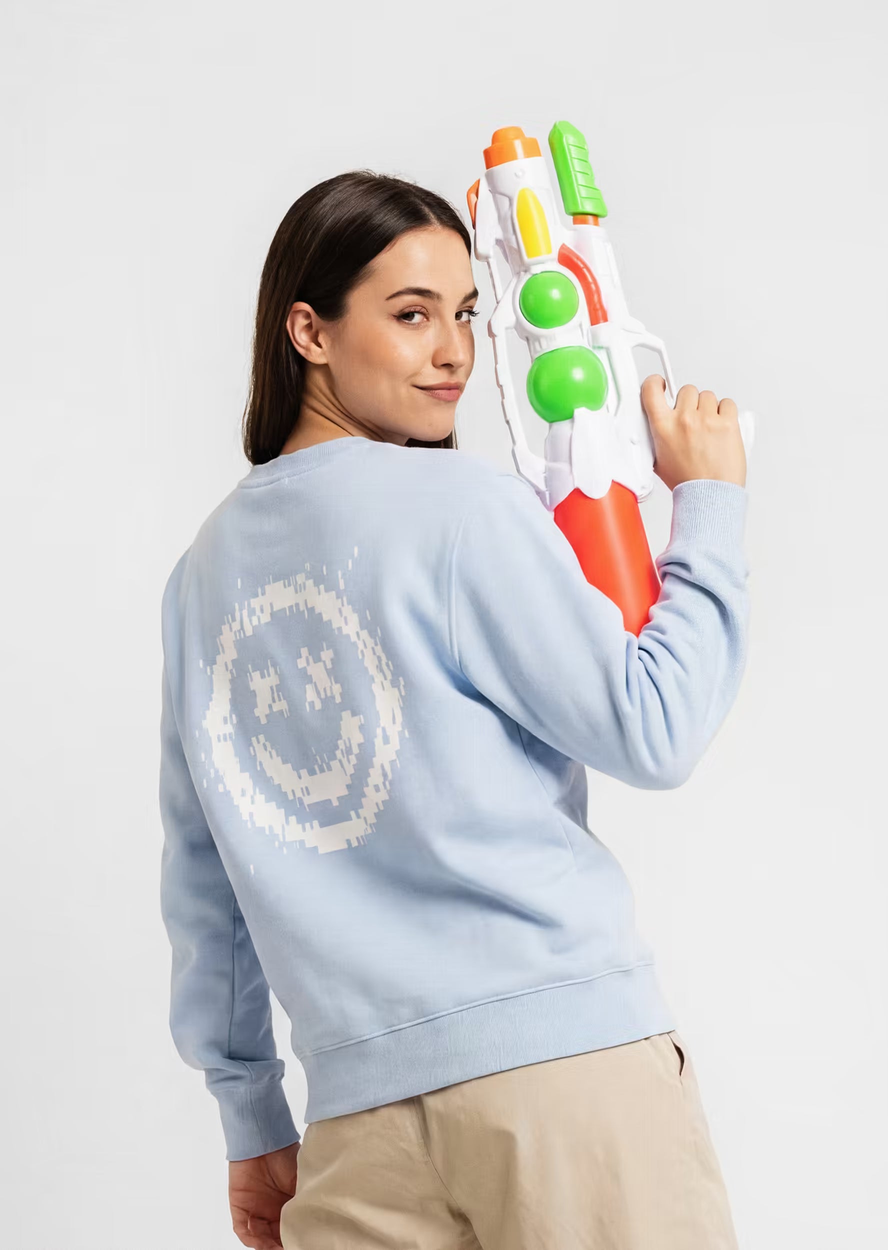 Modelo con sudadera Smiley Pixel Art Crystal Peppers azul celeste sosteniendo una pistola de agua — serigrafía pixel art blanca en la espalda